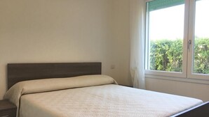 Ein Schlafzimmer mit einem Bett, einem Nachttisch und einem Fenster mit Blick auf Grünflächen.