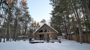 Een houten chalet met terras, omringd door hoge bomen en bedekt met sneeuw.