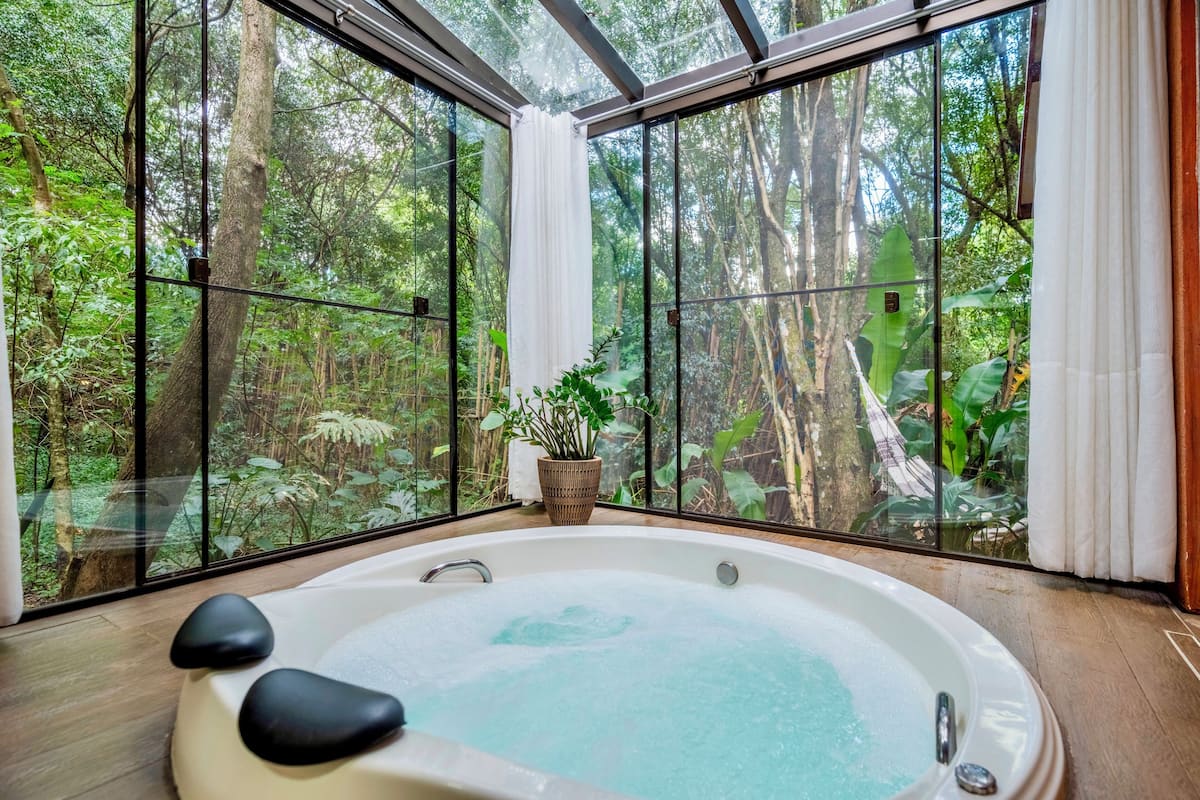 A spa room with a hot tub, large windows, and a view of a forest.