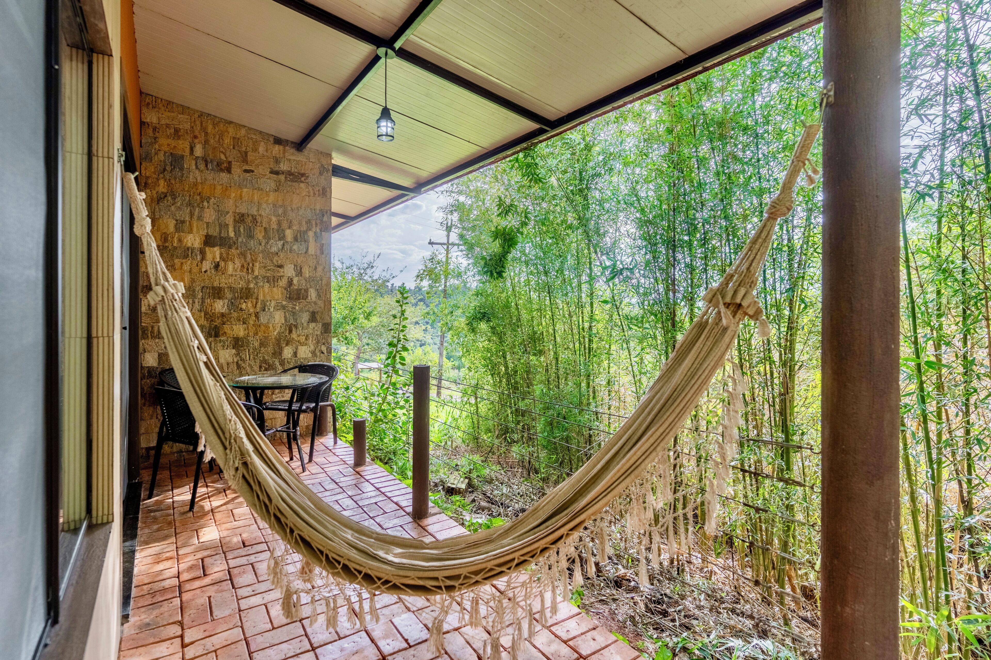 A hammock on a brick patio with a stone wall and a view of bamboo forest.