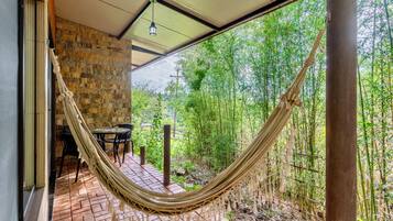 A hammock on a brick patio with a stone wall and a view of bamboo forest.