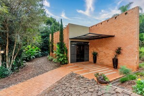 A brick building with a covered entrance, surrounded by greenery and a paved pathway. - Hotel Fazenda Vale Alvorada (Cascavel)