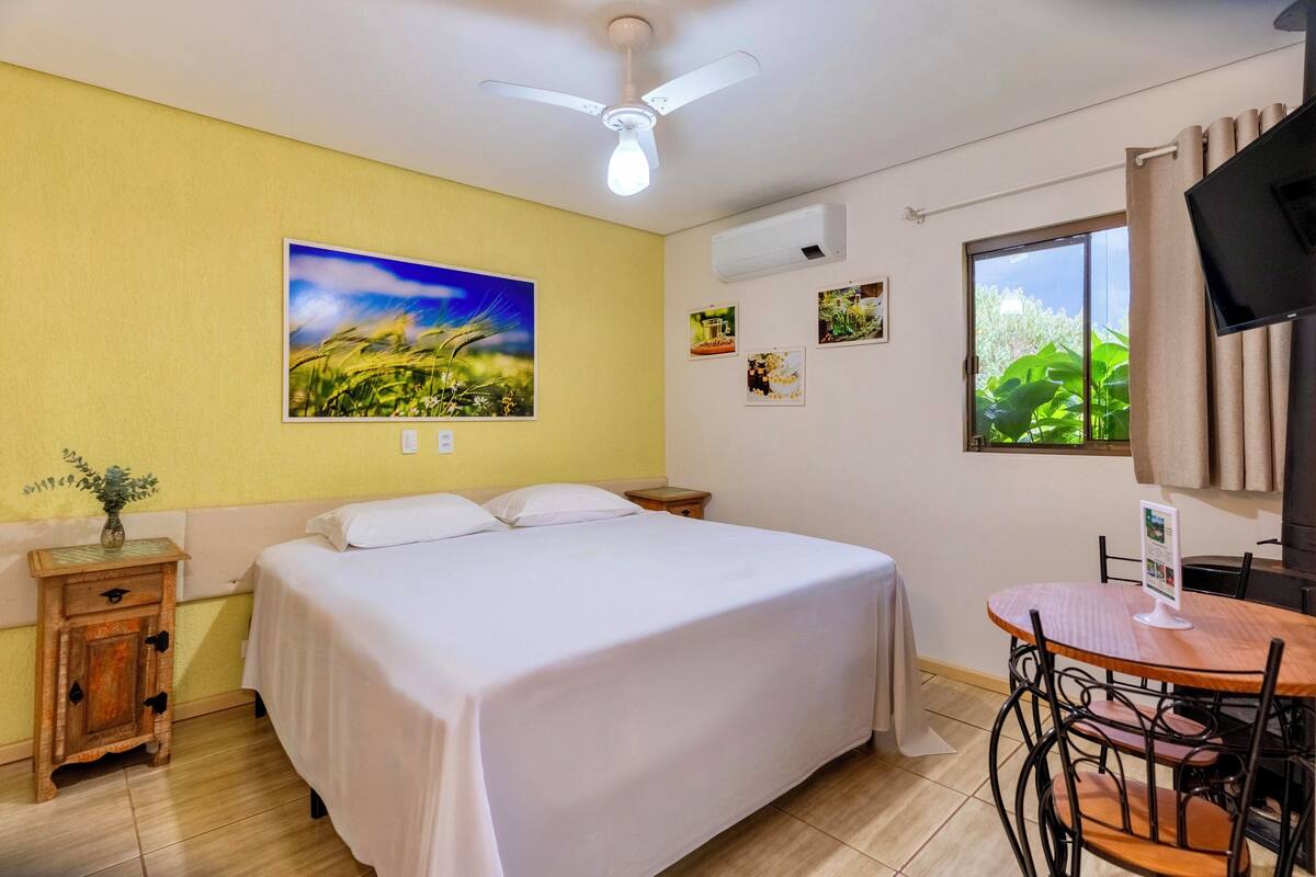 A bedroom with a bed, a small table, and chairs, a ceiling fan, and a window with curtains.