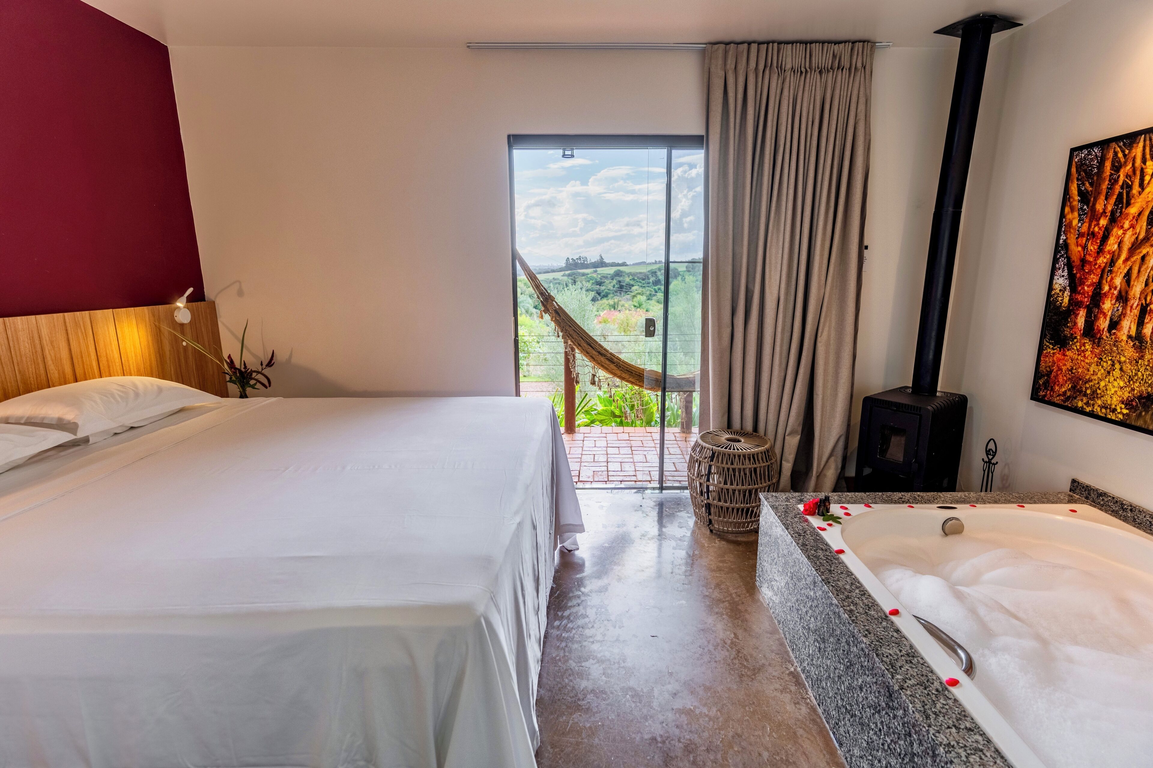Habitación de hotel con cama, bañera de hidromasaje, vista a follaje y chimenea.