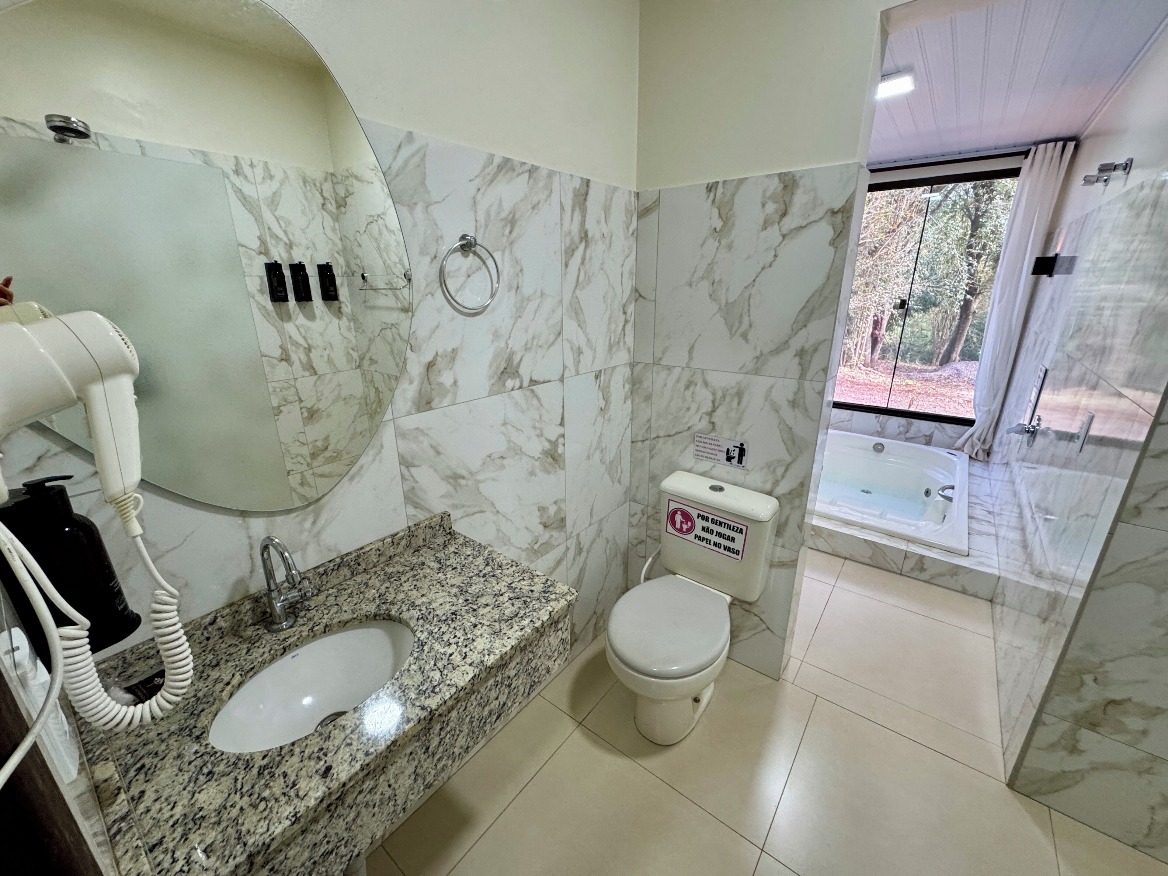 Baño con lavamanos de mármol, inodoro y zona de ducha con vistas.