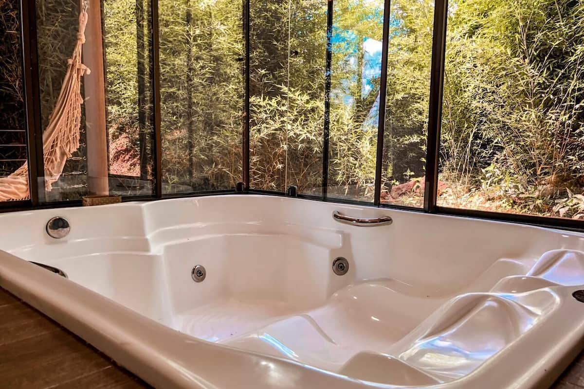 A white hot tub with a view of bamboo forest through large windows.