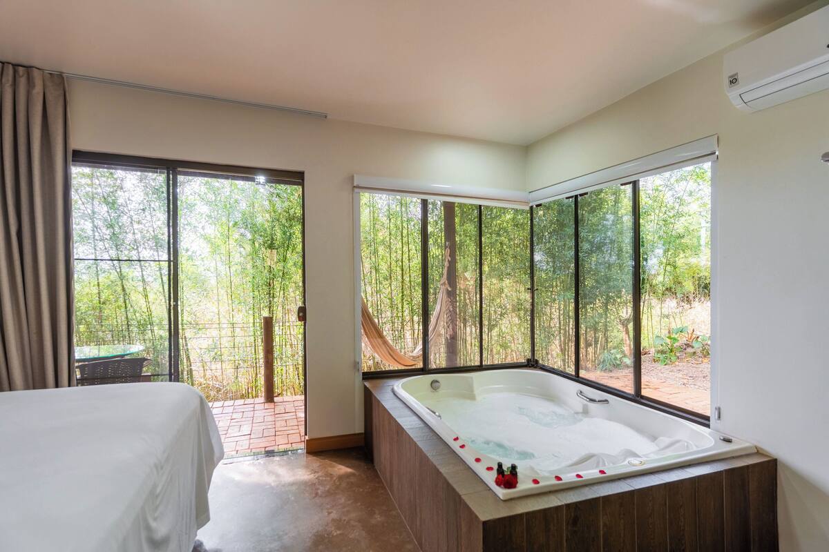 A bedroom with a large window, a bathtub, and a bed.