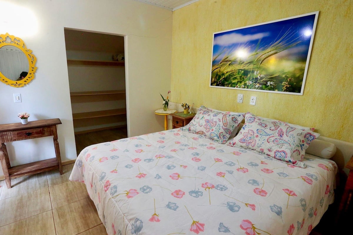 A bedroom with a bed, a bedside table, a mirror, a shelf, and a painting on the wall.