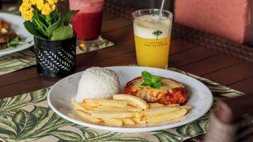 A plate with rice, a meat dish, and fries on a table with a drink and flowers in the background.