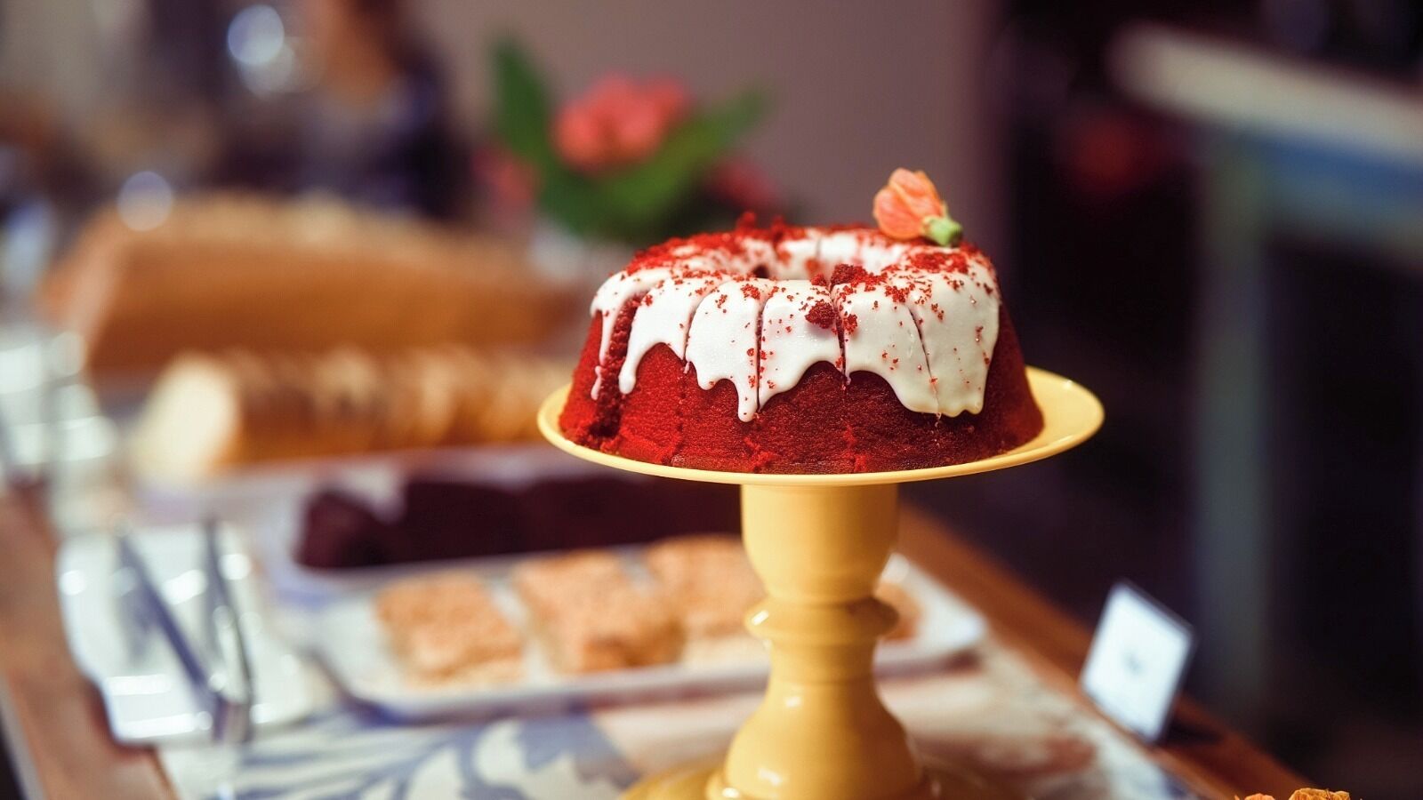 A dessert display with a red velvet cake topped with white icing and red sprinkles.