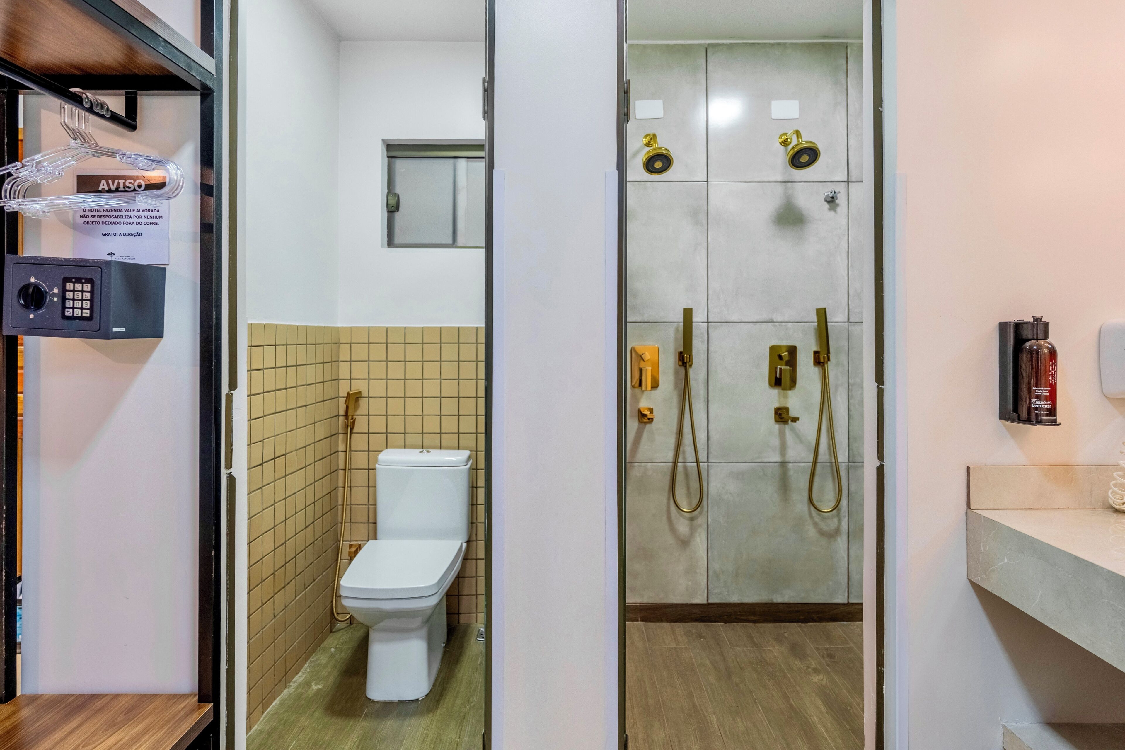A bathroom with a toilet, a shower with gold fixtures, and a security keypad.