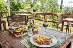 Mesa de jantar com prato de comida, taça de vinho e salada em um deck de madeira com cadeiras.