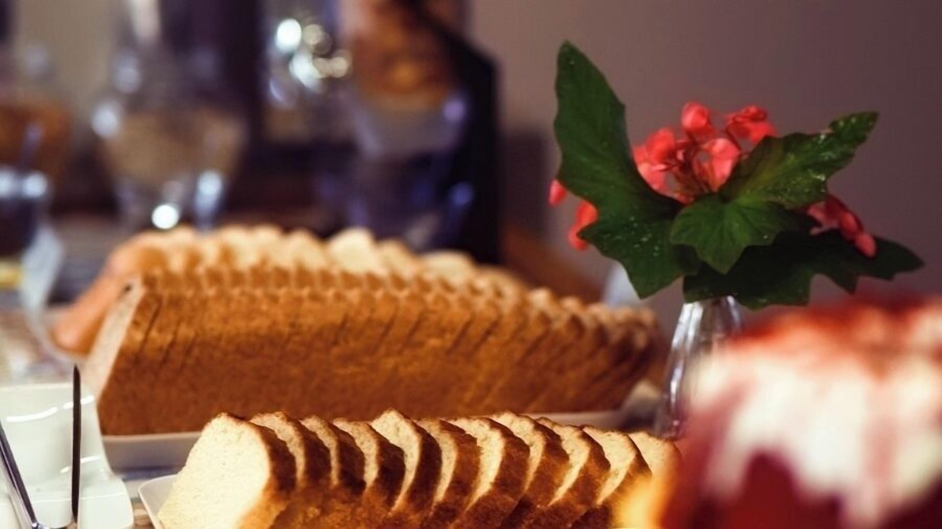 A loaf of sliced bread and a vase with red flowers on a table.