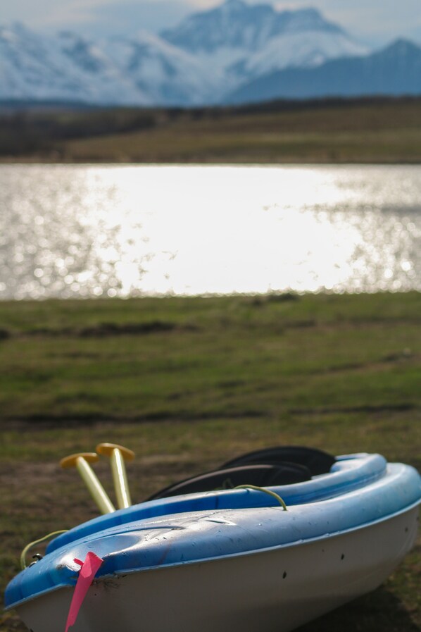 Un barco con diseño azul y blanco, ubicado en una zona verdejante cerca de un cuerpo de agua con montañas al fondo.