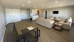 Een moderne woonkamer met een bank, salontafel en een eethoek met een tafel en stoelen. Er is ook een keuken met kastjes en een spoelbak.