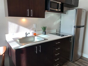 Una cocina con armarios oscuros, un refrigerador de acero inoxidable, un microondas, un fregadero y una pequeña planta en maceta.