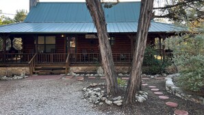 Eine rustikale Holzhütte mit Veranda, Kiesweg und umliegenden Bäumen.