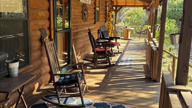 Eine Holzhütte mit Veranda, ausgestattet mit Schaukelstühlen, einem Tisch und einem Schild mit der Aufschrift 'Welcome to the Porch'.