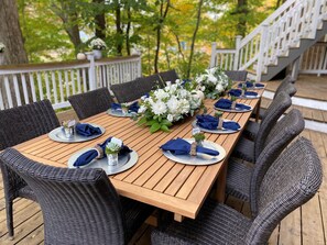 Eine Holzterrasse mit Esstisch, gedeckt für sechs Personen, umgeben von Korbstühlen.