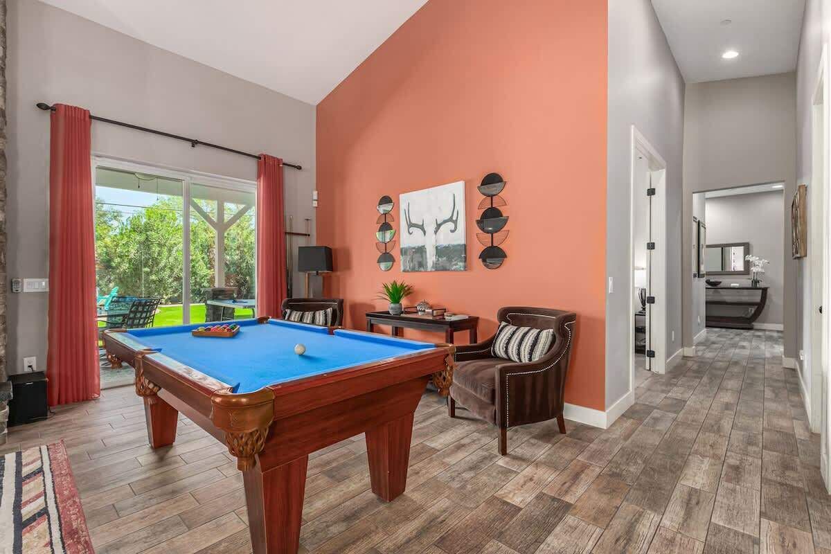 Une table de billard dans une pièce avec vue, une chaise et un mur décoré d’objets.