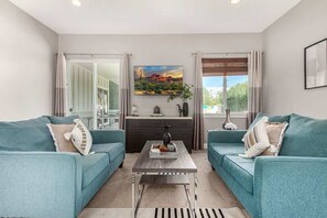 A modern living room with teal sofas, a coffee table, and a painting of a desert landscape.
