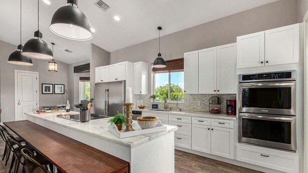A modern kitchen with white cabinets, a large island, pendant lights, and stainless steel appliances.