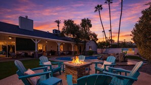 An outdoor seating area with chairs and a fire pit, surrounded by a pool and a covered patio.