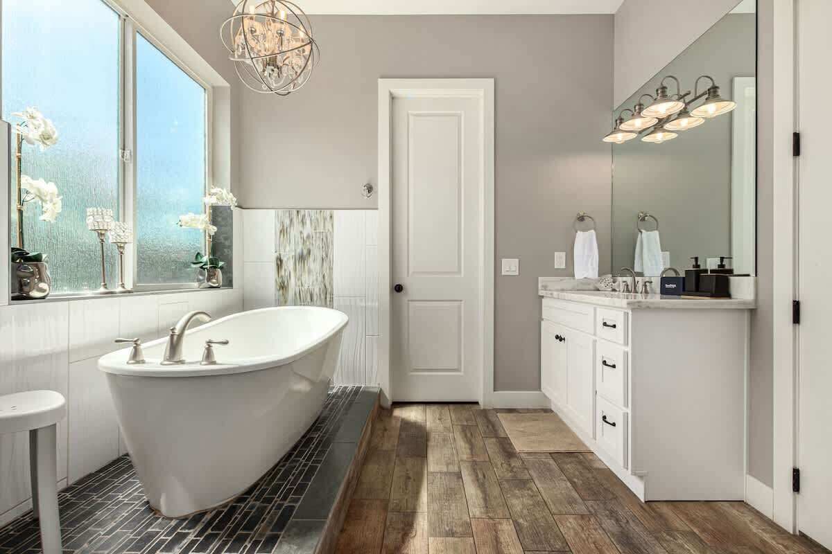 A modern bathroom with a freestanding bathtub, a large mirror, and a window with flowers.