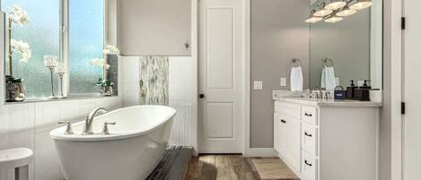 A modern bathroom with a freestanding bathtub, a large mirror, and a window with flowers.