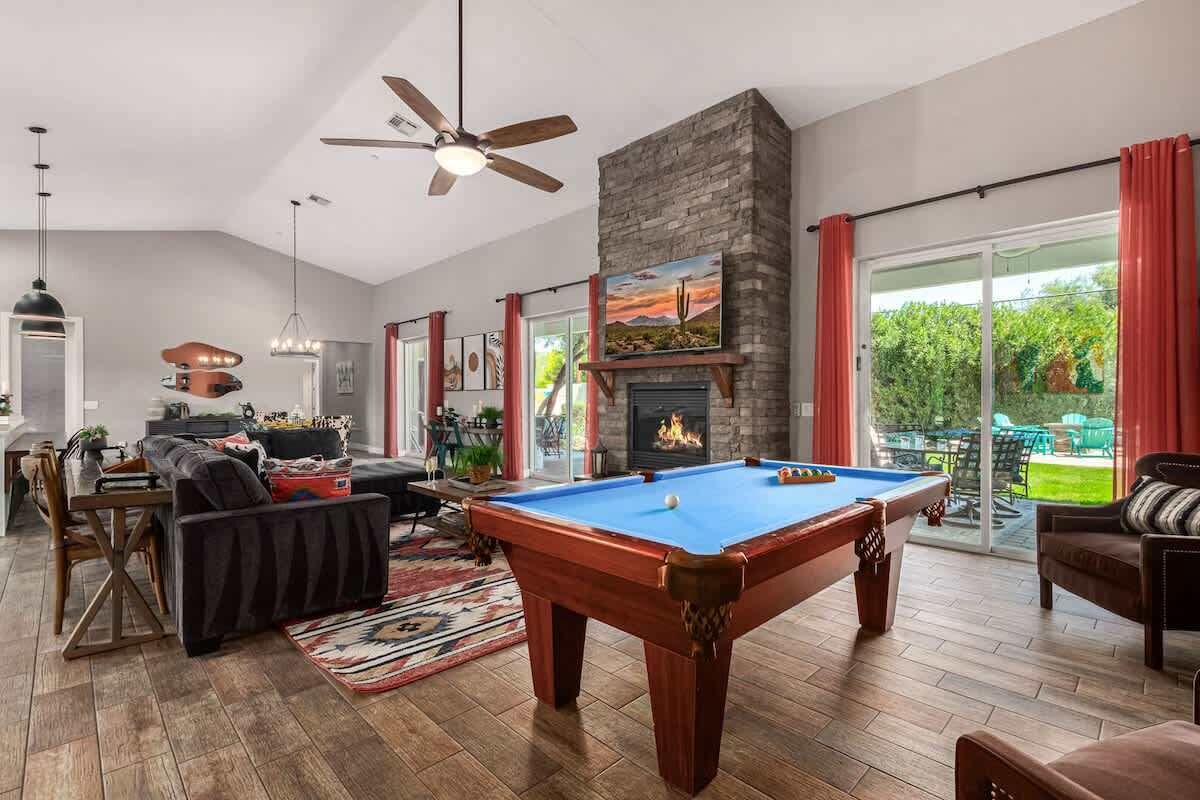 Une table de billard dans un salon avec une cheminée, un ventilateur de plafond et un coin repas.