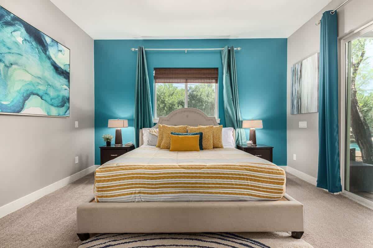 A bedroom with a bed, two bedside tables, a window with curtains, and a view of trees.