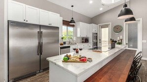 A modern kitchen with stainless steel appliances, a marble island, and pendant lighting.