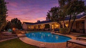 A backyard with a swimming pool, a covered patio, and a house.