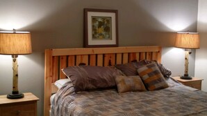 A bedroom with a wooden headboard, a bed with patterned bedding, two bedside tables with lamps, and a framed picture on the wall.