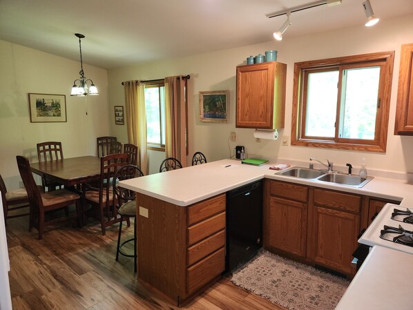 Una cocina con alacenas de madera, lavavajillas, estufa y un comedor con sillas y mesa.