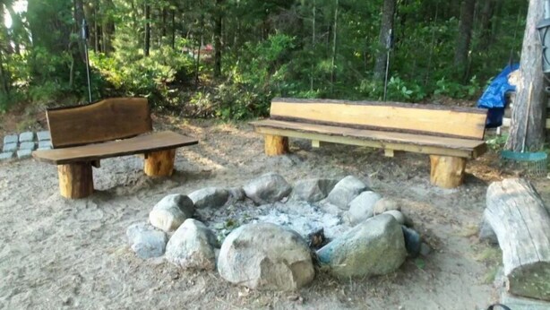 A forested area with two wooden benches and a stone fire pit.