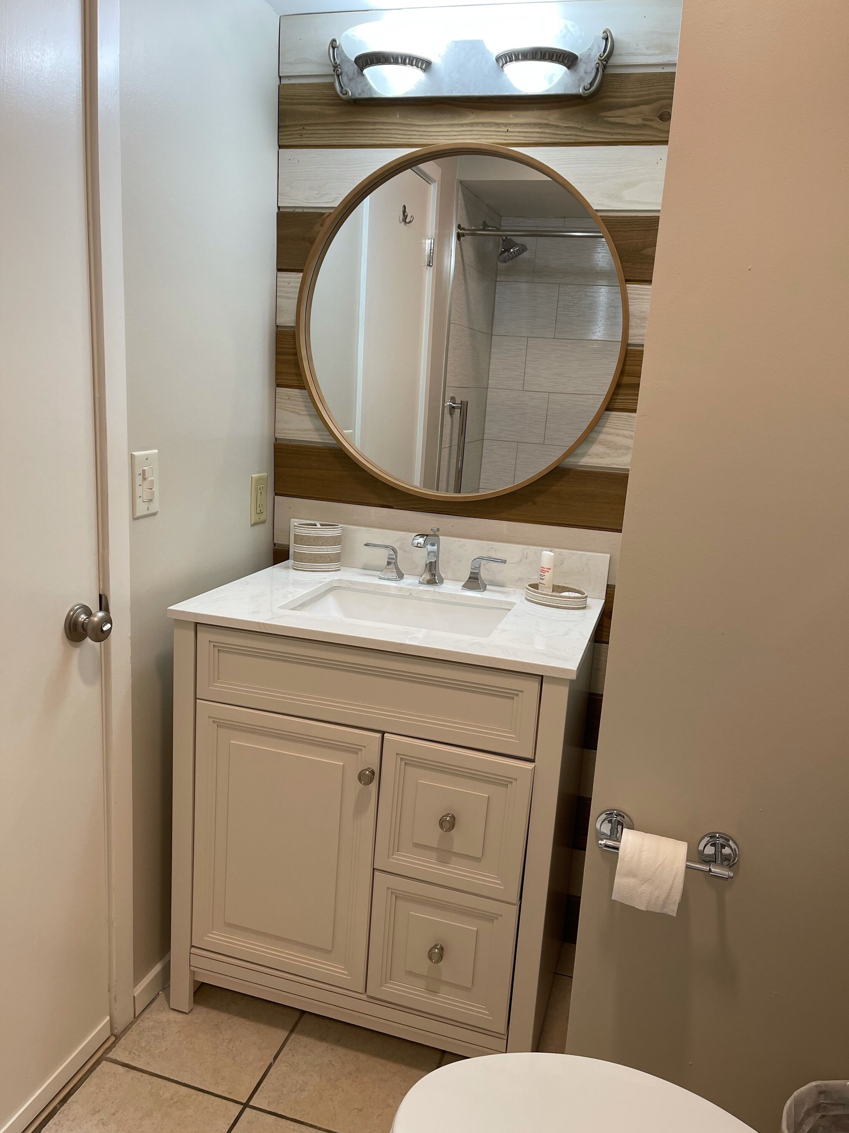 Een badkamer met een witte wasbak, een ronde spiegel en een douchegedeelte.