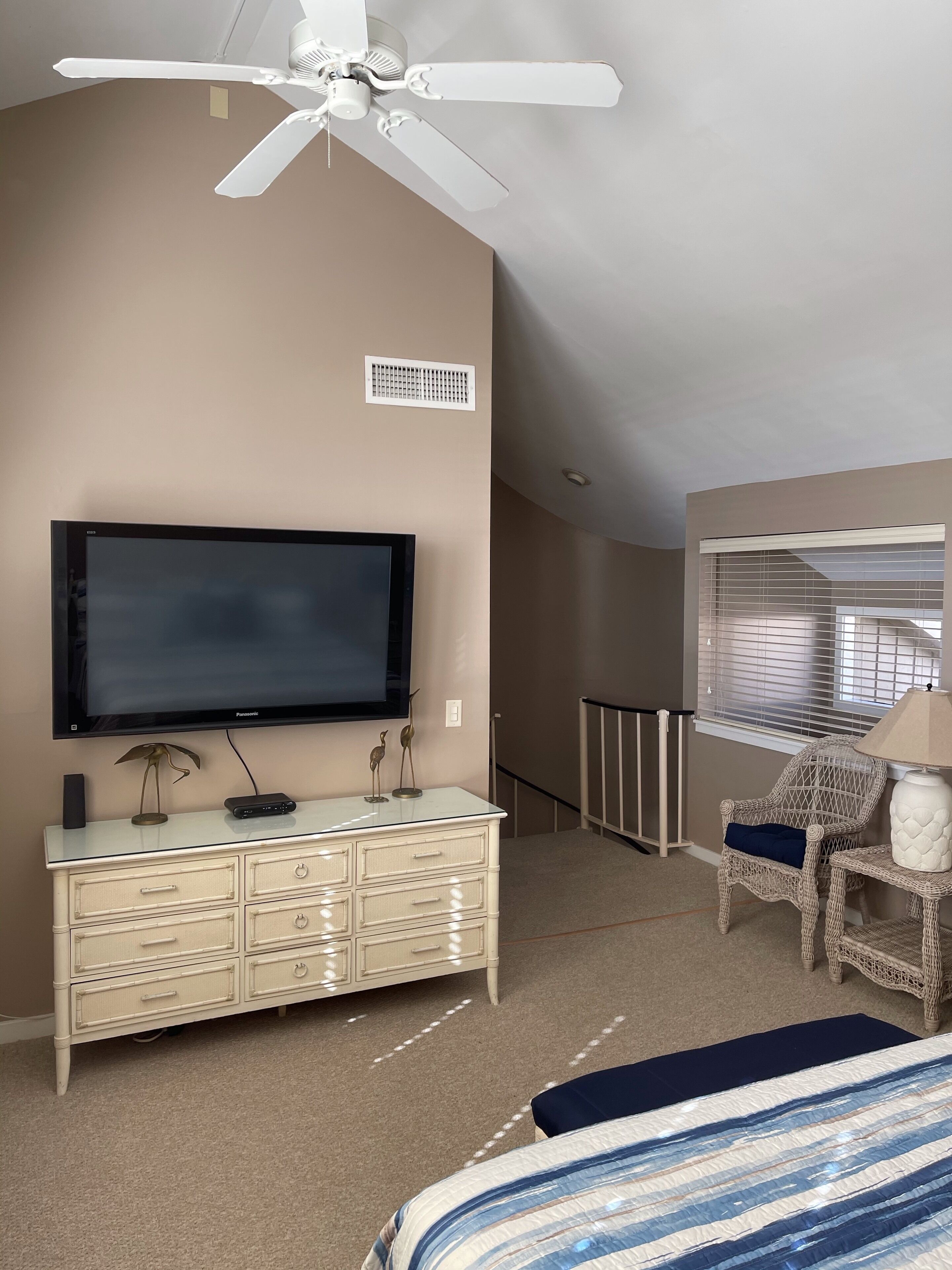 A bedroom with a ceiling fan, a television, a dresser, a chair, and a window with blinds.
