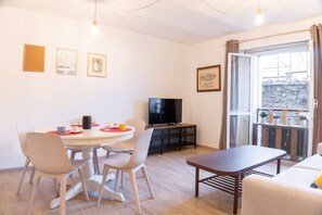 A modern living room with a dining table, chairs, a flat-screen TV, and a balcony with potted plants.
