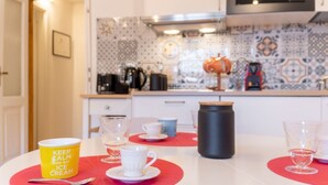 Ett kök med kakel på väggen ovanför arbetsbänken, en mikrovågsugn, en kaffebryggare och en vattenkokare på bänken.