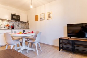 A modern kitchen with a microwave, dining table, chairs, and a TV on a stand.