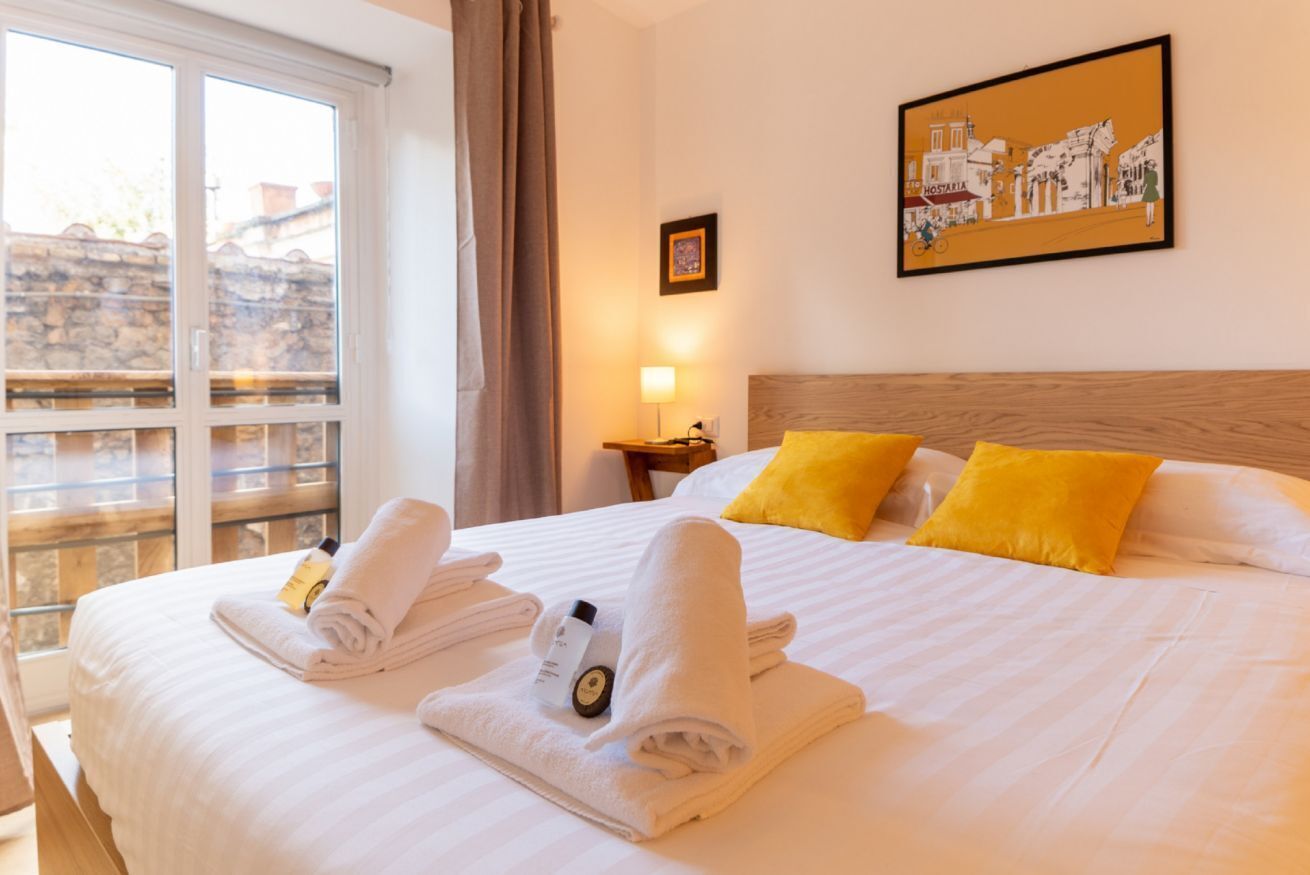 Una camera d'hotel con un letto, due cuscini, una finestra, un quadro al muro e un comodino con una lampada.