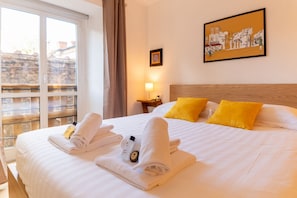 A hotel room with a bed, two pillows, a window, a picture on the wall, and a nightstand with a lamp.