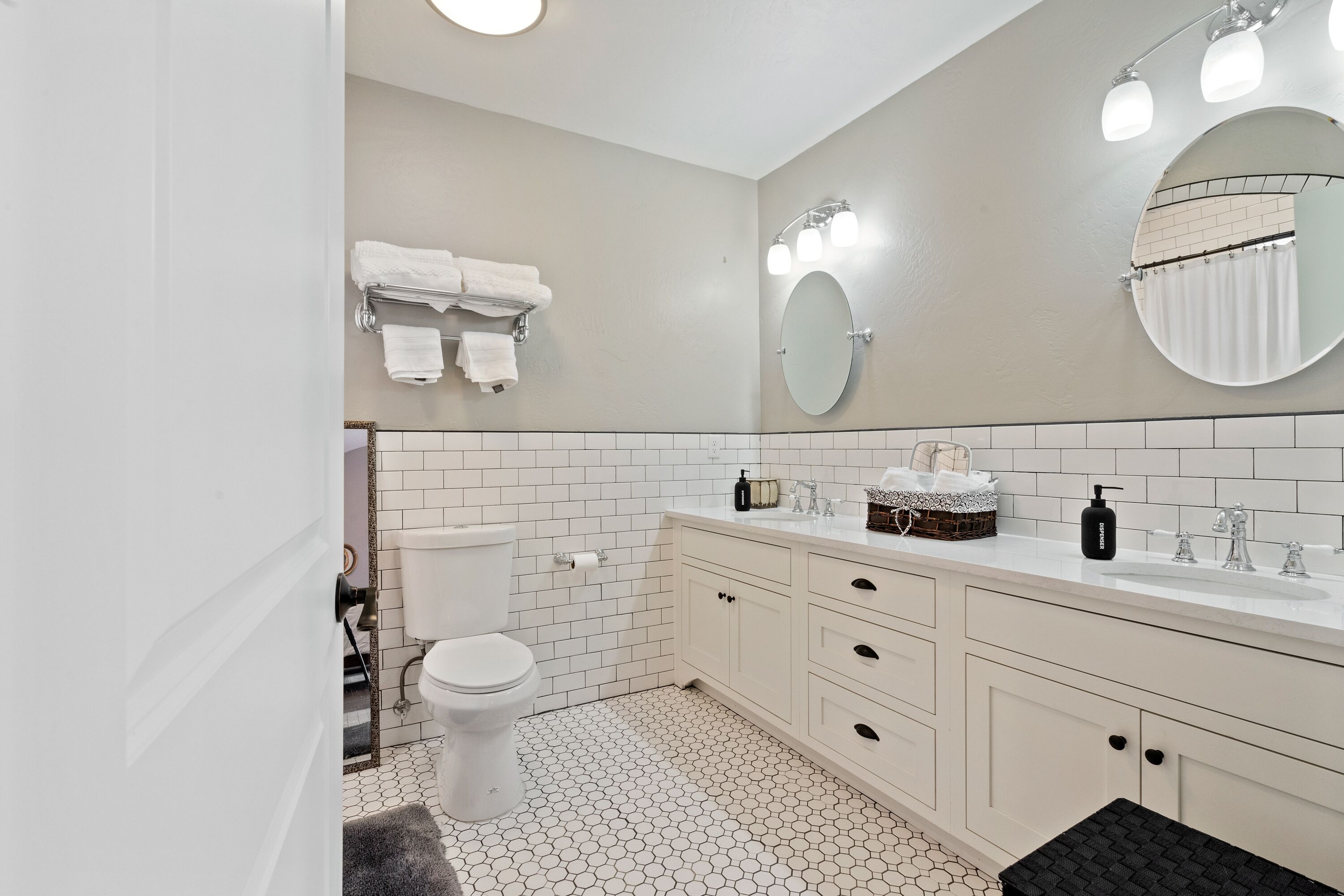 Une salle de bain avec des toilettes, un lavabo et un miroir. Des serviettes sont suspendues sur un porte-serviettes et un panier est posé sur le comptoir du lavabo.