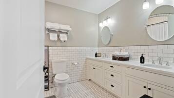 Une salle de bain avec des toilettes, un lavabo et un miroir. Des serviettes sont suspendues sur un porte-serviettes et un panier est posé sur le comptoir du lavabo.