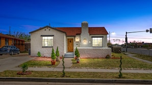 A single-story house with a red roof, white exterior walls, and a front porch. There are small potted plants in the front yard.