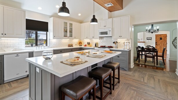 A modern kitchen with a large island, white cabinetry, and a herringbone wood floor.