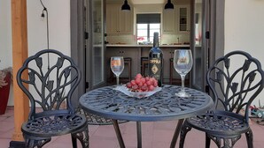 An outdoor dining area with a round table and four chairs, a bottle of Coppelia wine, and a glass of wine on the table.