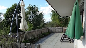 Un patio con valla de madera, mobiliario exterior y sombrillas.