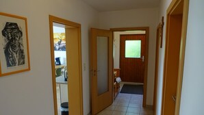 Un pasillo con puertas de madera, piso de baldosas y una obra de arte enmarcada en la pared.